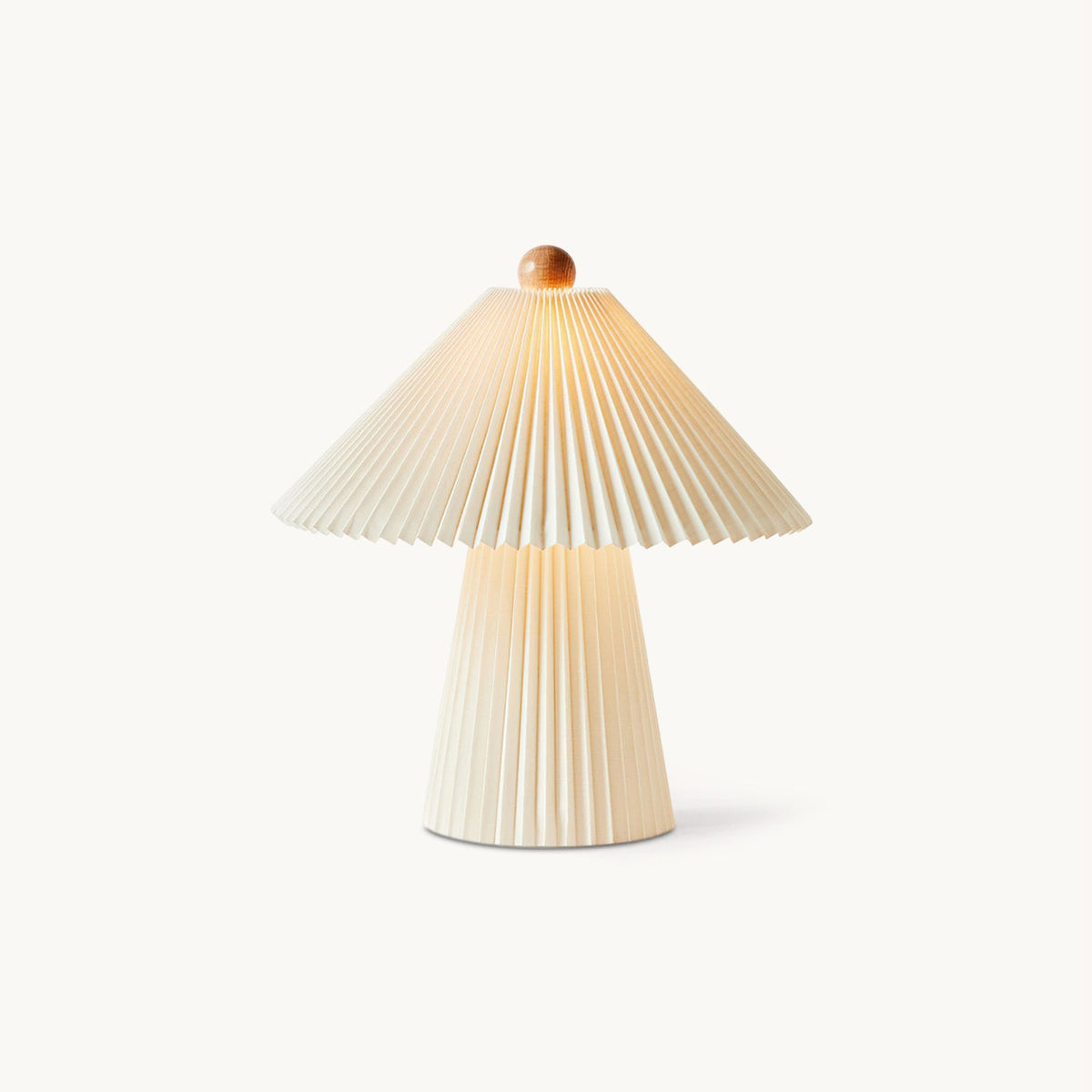 Cut-out view of a Clérachic table lamp with a pleated beige conical shade, a wooden finial and a tapered pleated base, on white.