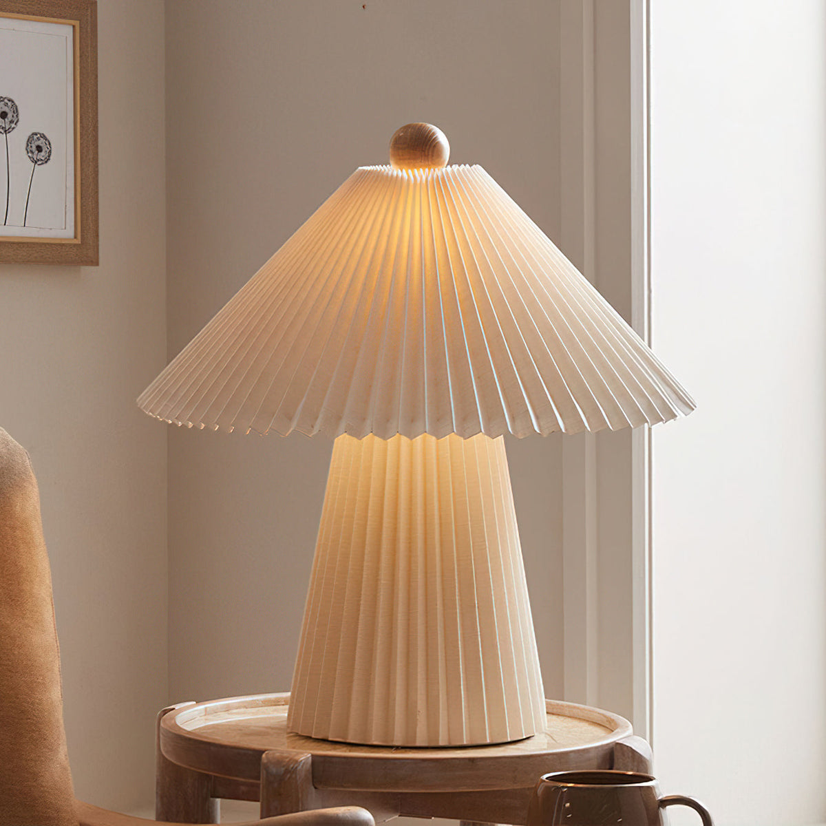 Close view of the lit pleated conical shade and wooden finial of this Clérachic table lamp, above its glowing pleated base.