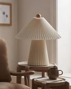 A cooler, grey-toned version of this Clérachic table lamp, unlit, on a round wooden side table beside a brown mug.