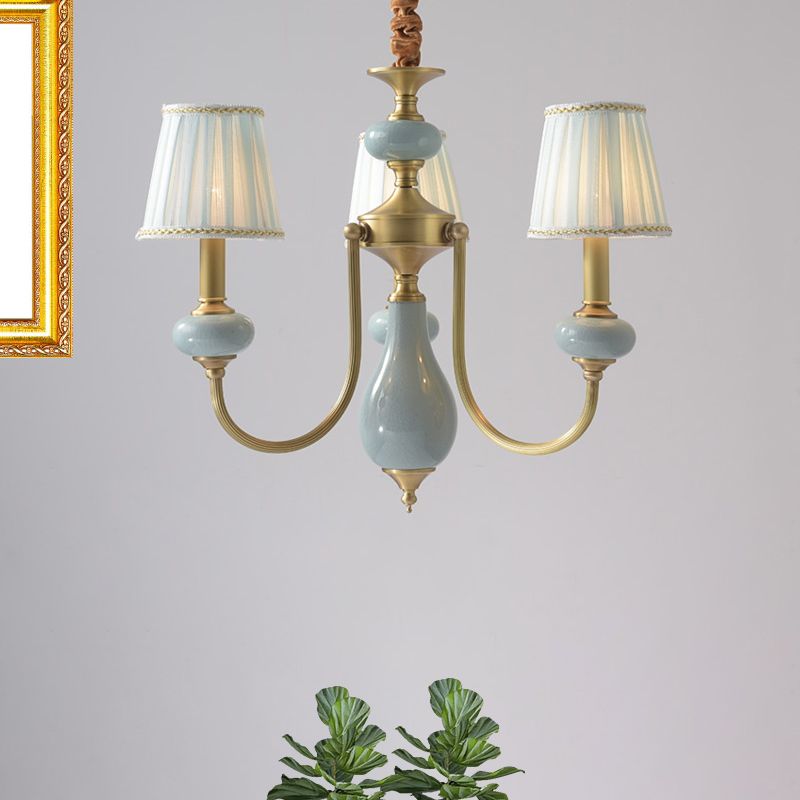 Three-arm Pleated Blue Fabric Chandelier from Clérachic, showing pleated shades, brass arms and a glazed ceramic centre column.