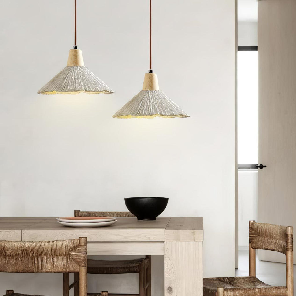 Two Clérachic pendants with pleated grey shades glow above a pale wooden table, beside woven-seat chairs and a black bowl.