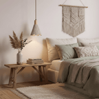 A small bell-shaped Clérachic pendant glows beside a bed with sage bedding, pampas grass and a macramé hanging on the wall.