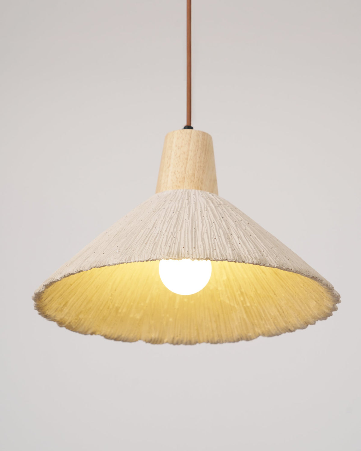 A cream-toned version of this Clérachic pendant, lit with a bulb visible inside its yellow-tinted shade and a wooden cap above.