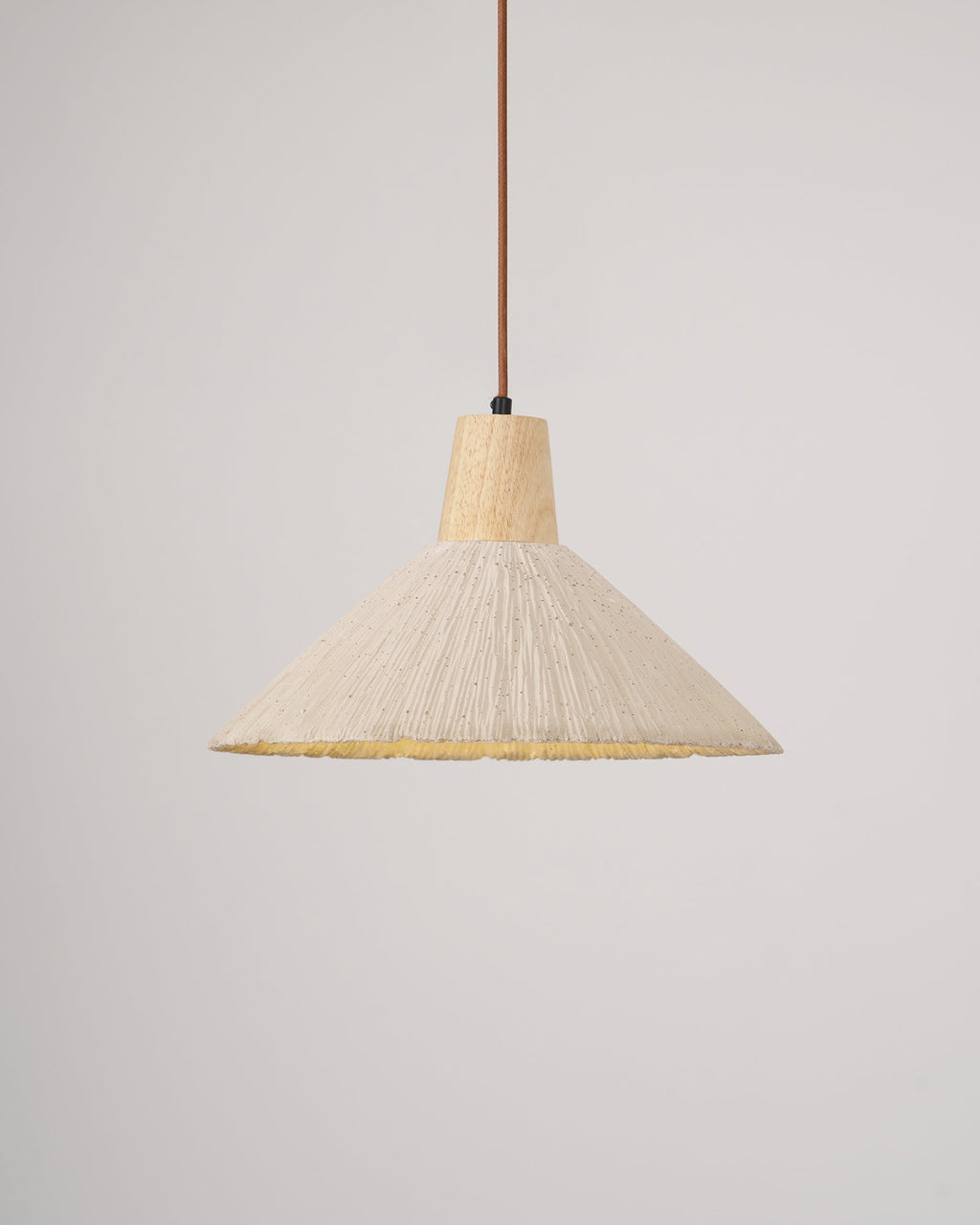 The same cream-toned Clérachic pendant switched on, its pleated rim glowing yellow beneath the shade.