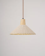 The same cream-toned Clérachic pendant switched on, its pleated rim glowing yellow beneath the shade.