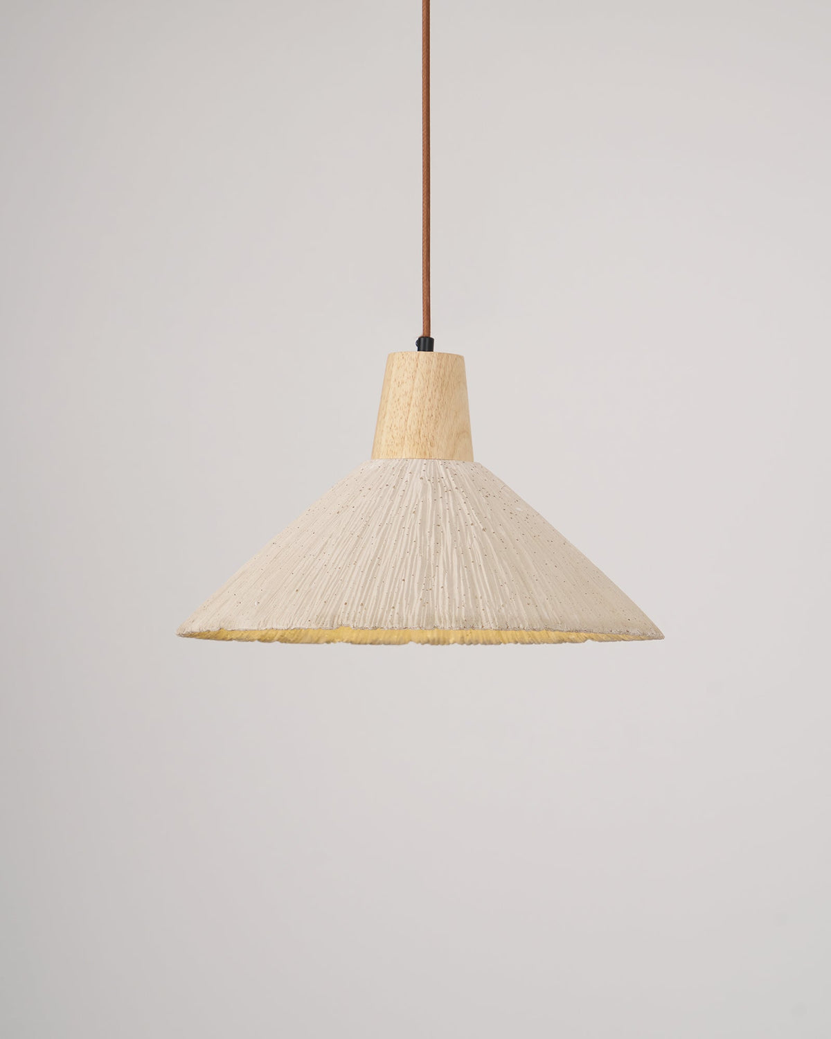 The same cream-toned Clérachic pendant switched on, its pleated rim glowing yellow beneath the shade.