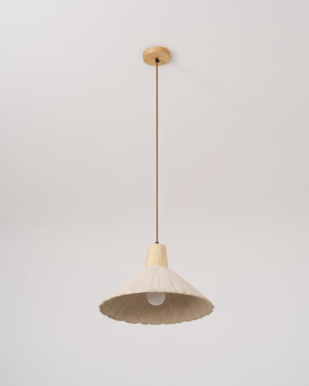 A cream-toned Clérachic pendant on a round wooden canopy, hanging low with its bulb showing inside the shade.