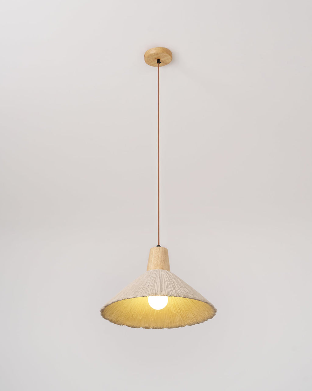 A cream-toned Clérachic pendant on a wooden canopy, lit warm, with its bulb and pleated rim against a plain backdrop.