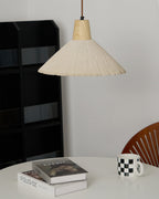 A cream-toned Clérachic pendant hangs over a white table with art books and a checked mug, beside a black shelf and a wooden chair.