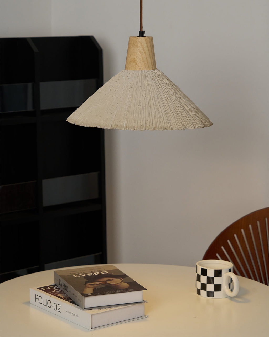 The same cream-toned Clérachic pendant switched on, warming a white table with books and a black and white checked mug.