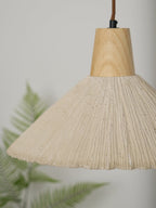 Close view of a cream-toned Clérachic pendant, its fine pleats and wooden cap in focus against a soft green fern.