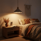 A Clérachic pendant with a darker grey shade casts amber light over a bedside table and a rust-coloured throw in a dim bedroom.