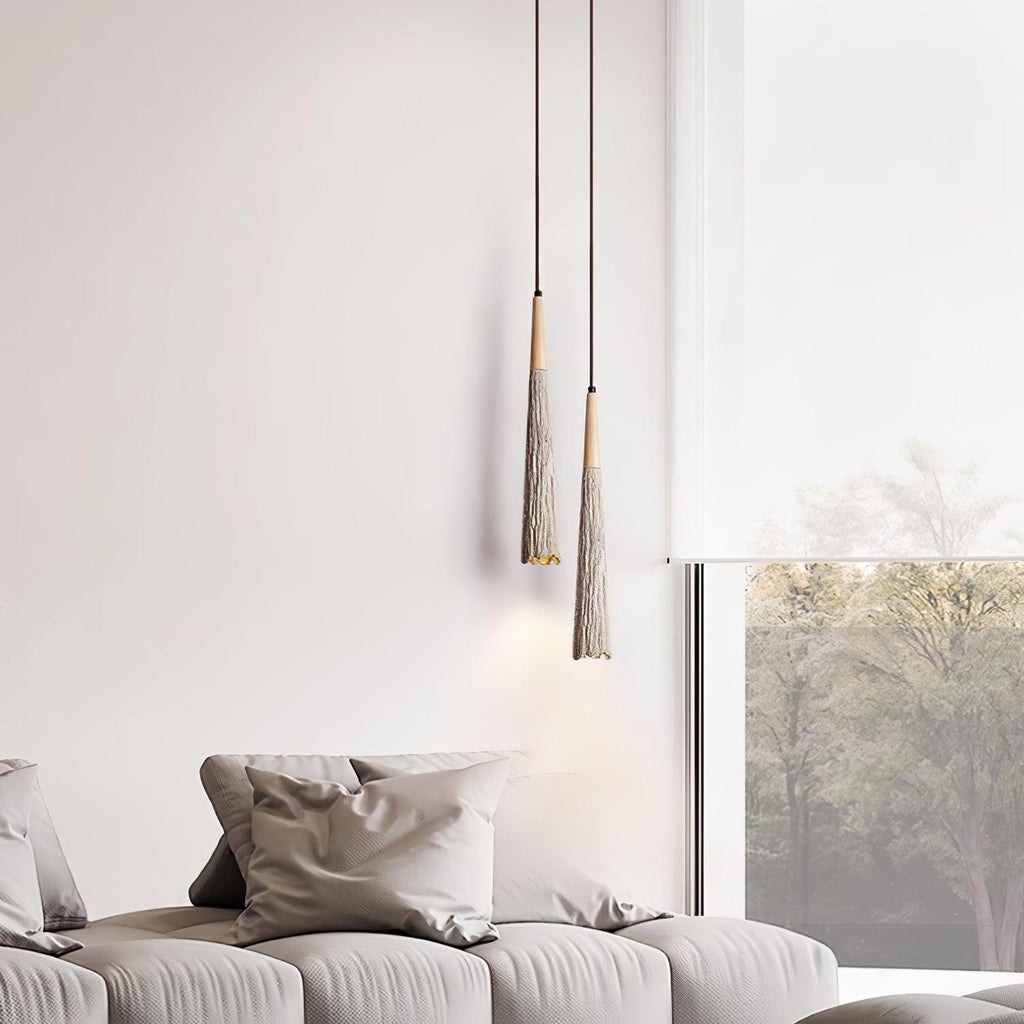 Two slim, tapered Clérachic pendants with fringed-looking shades hang beside a grey sofa and a tall window.