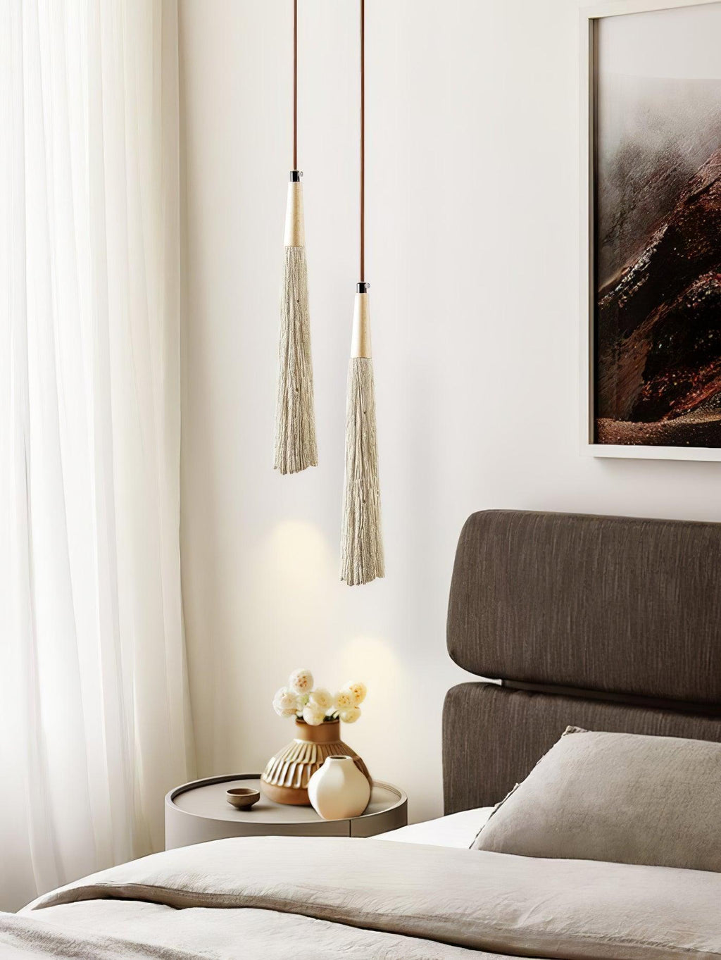Slim tapered Clérachic pendants with gold-toned tops hang beside a bed, near a curtain and a small table with flowers.