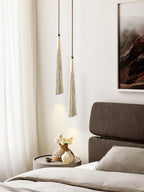 Slim tapered Clérachic pendants with gold-toned tops hang beside a bed, near a curtain and a small table with flowers.