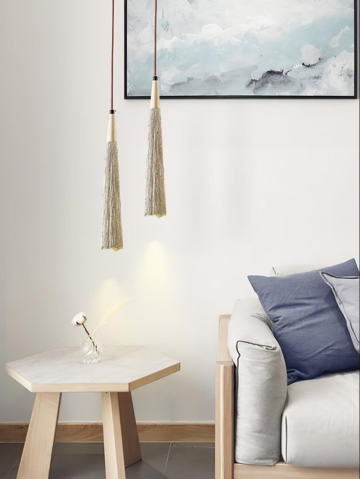 A pair of narrow Clérachic pendants hang over a hexagonal pale-wood side table, with an armchair and a blue-toned painting behind.
