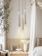 Three narrow Clérachic pendants hang together beside a window with a draped white canopy and a slatted wall panel.