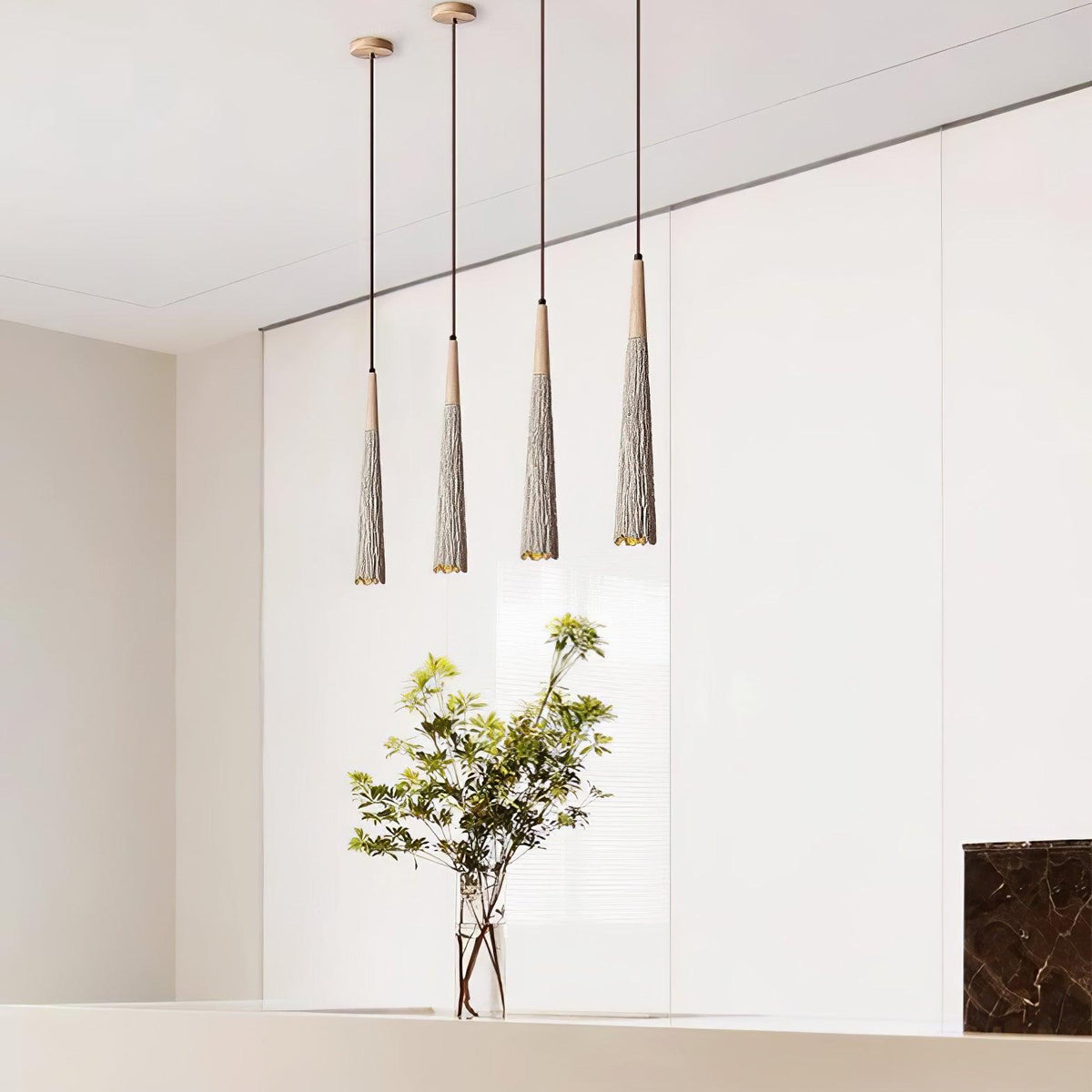 A row of four slim Clérachic pendants hangs against a white wardrobe wall, with a leafy plant in a glass vase below.