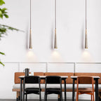Three slim Clérachic pendants hang evenly over a dining bench and table, each throwing a small pool of light on the wall.