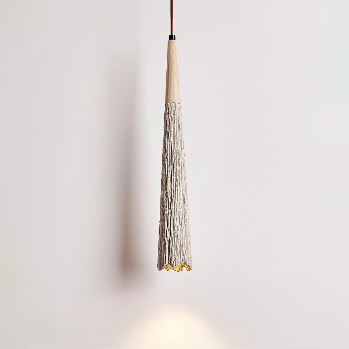Close view of the slim tapered shade on this Clérachic pendant, with a wooden collar and a warm glow at the tip.