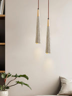 Two slim Clérachic pendants hang beside a bookshelf and a leafy plant, each lighting a small patch of wall.