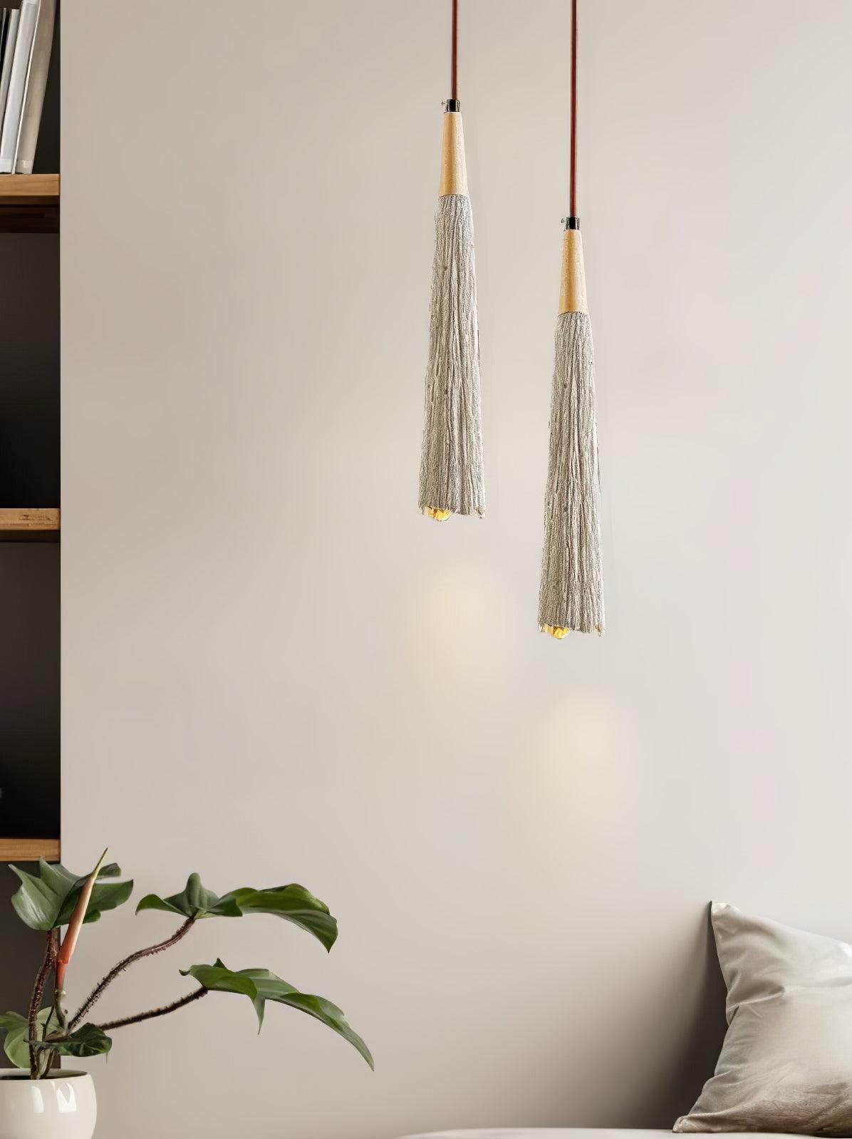 Two slim Clérachic pendants hang beside a bookshelf and a leafy plant, each lighting a small patch of wall.