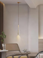 One slim Clérachic pendant hangs by a rattan lounge chair, with a small plant on a side table in the corner.
