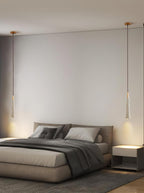 Two slim Clérachic pendants hang over a bed with grey bedding, one either side of the headboard wall.