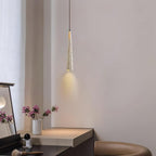 A slim Clérachic pendant lights a dark dressing table with a small vase of pink flowers beside it.