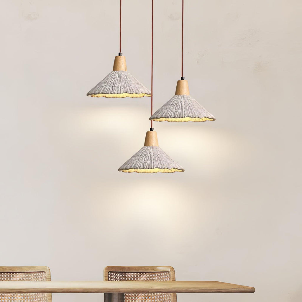 Three wide-cone Clérachic pendants hang in a cluster above a pale wooden dining table with rattan chairs.
