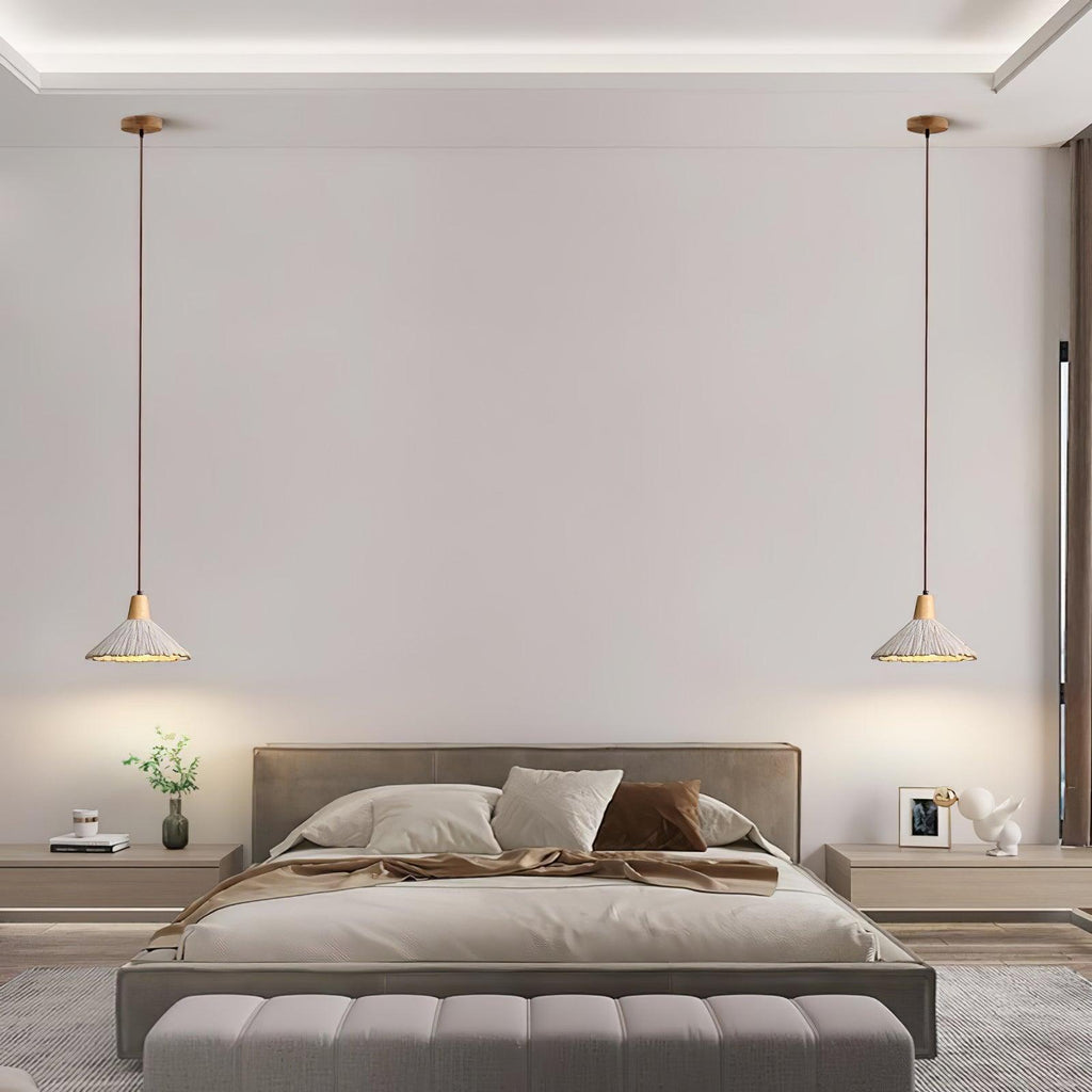 Two wide-cone Clérachic pendants hang either side of a bed in a pale room with a wide upholstered bench at its foot.