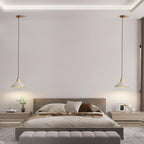 Two wide-cone Clérachic pendants hang either side of a bed in a pale room with a wide upholstered bench at its foot.
