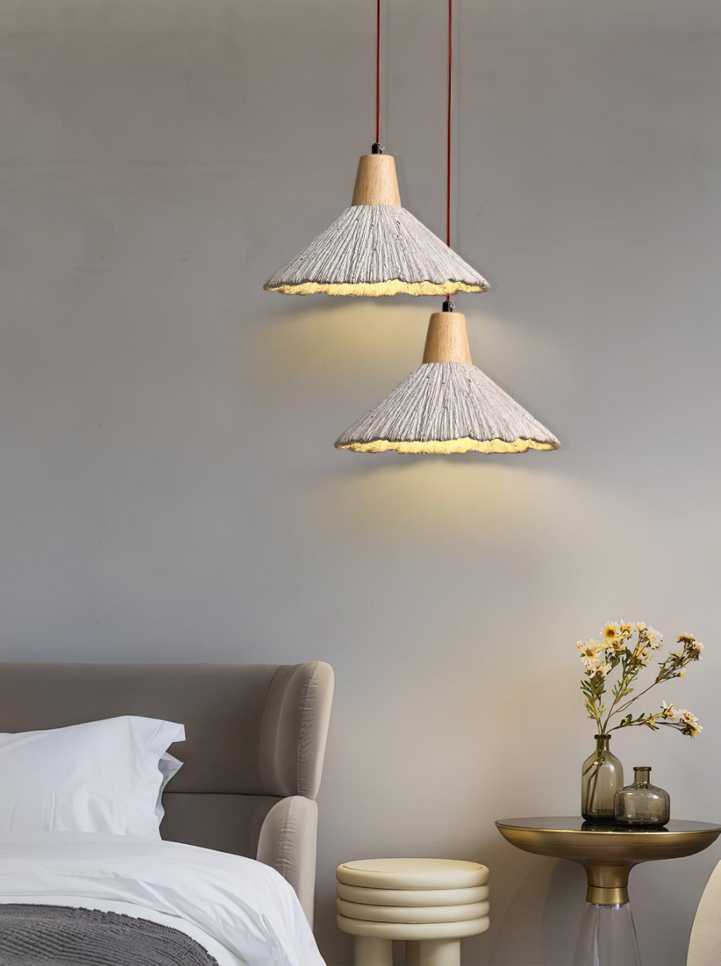 Two wide-cone Clérachic pendants hang one above the other beside a bed, near a gold side table with yellow flowers.