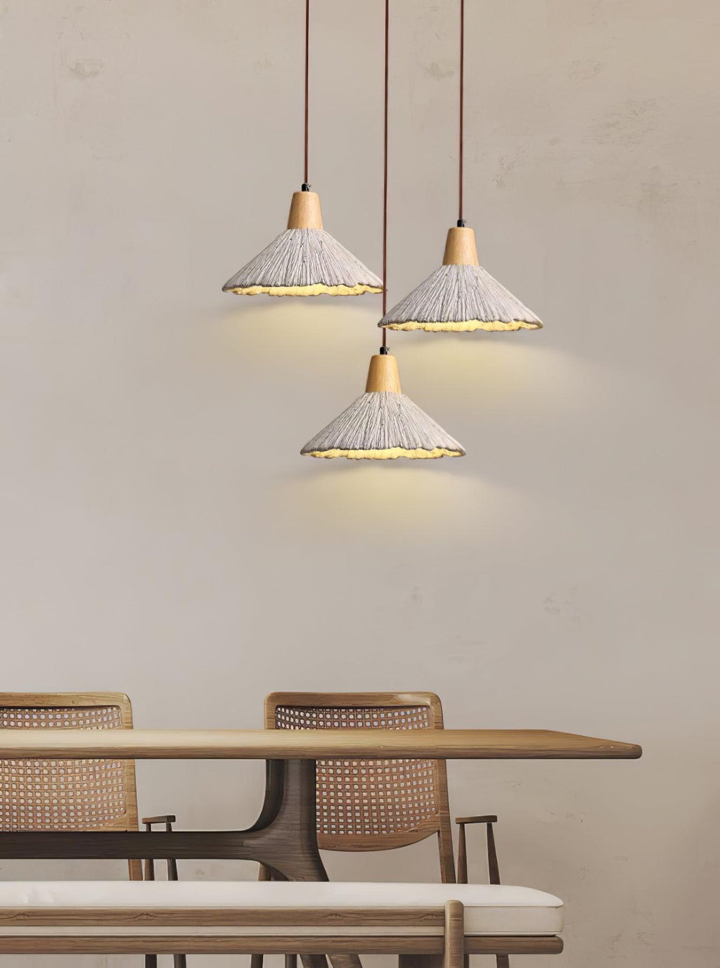 Three Clérachic pendants with wide shades hang at staggered heights over a dining table with rattan chairs.