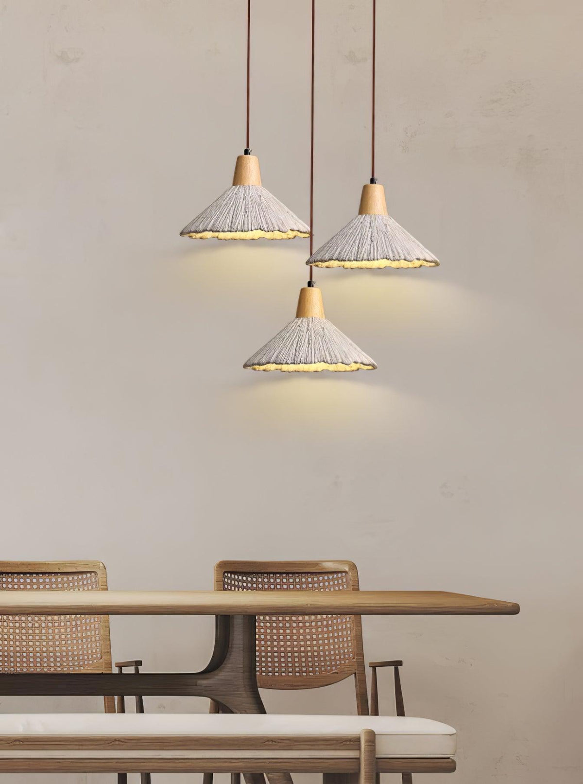 Three Clérachic pendants with wide shades hang at staggered heights over a dining table with rattan chairs.