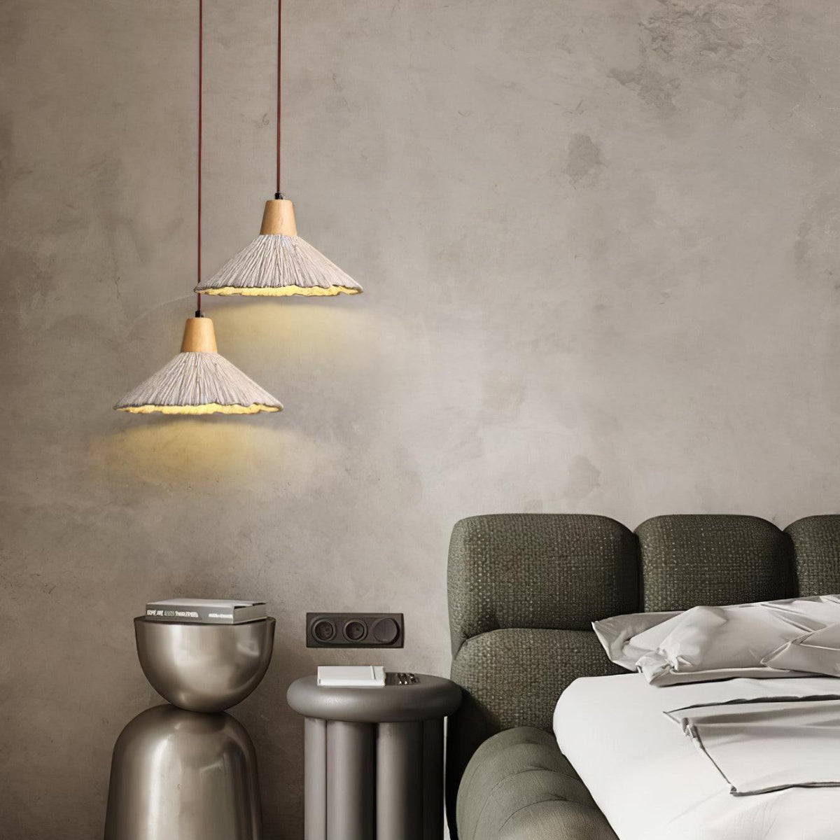 Two wide Clérachic pendants hang at different heights against a textured plaster wall, beside an olive-green sofa.