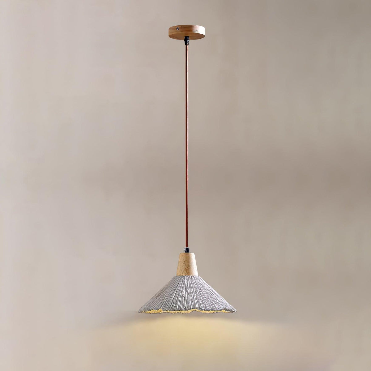A single Clérachic pendant on a round wooden canopy glows against a beige wall, its grey shade lit from within.