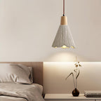 A bell-shaped Clérachic pendant hangs above a bedside shelf with a bud vase, with light washing up the wall behind.