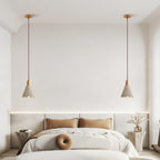 A pair of bell-shaped Clérachic pendants hang on wooden canopies above a bed with tan cushions.