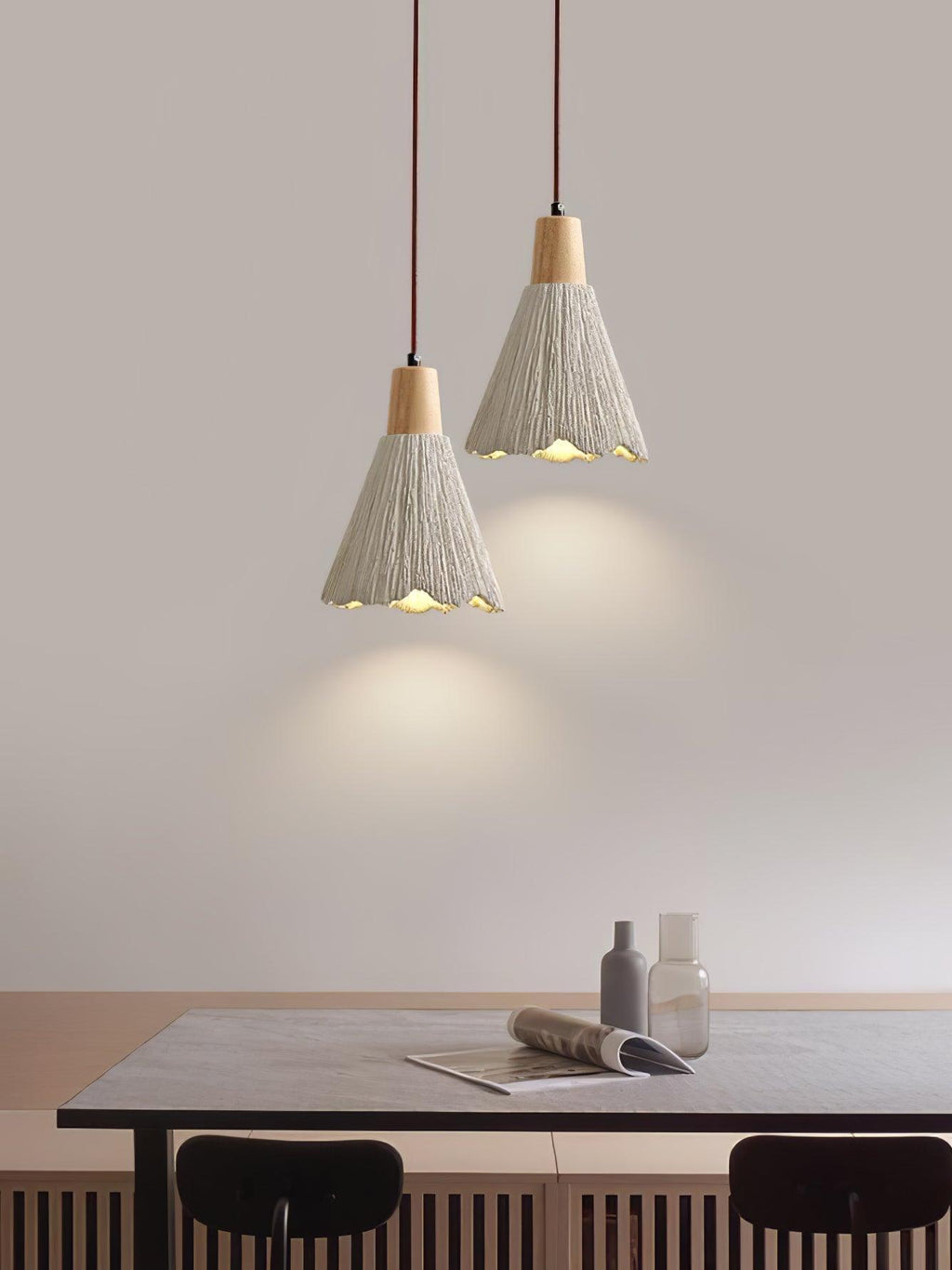Two bell-shaped Clérachic pendants hang above a dark dining table with a magazine and glass bottles on it.