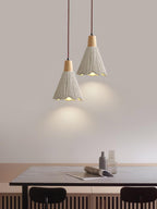 Two bell-shaped Clérachic pendants hang above a dark dining table with a magazine and glass bottles on it.