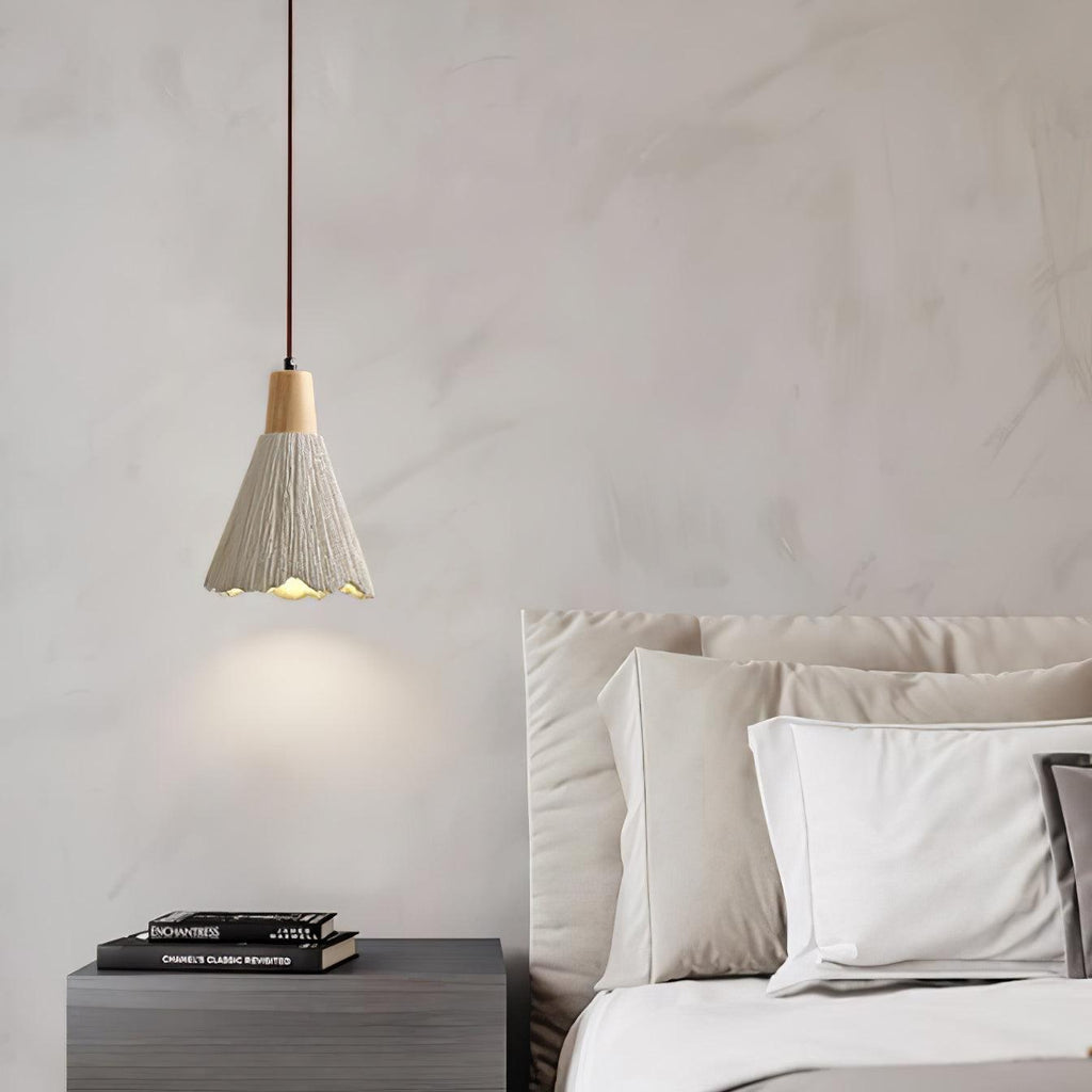 A single bell-shaped Clérachic pendant lights a marbled wall above a dark nightstand and a bed with white pillows.