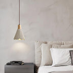 A single bell-shaped Clérachic pendant lights a marbled wall above a dark nightstand and a bed with white pillows.