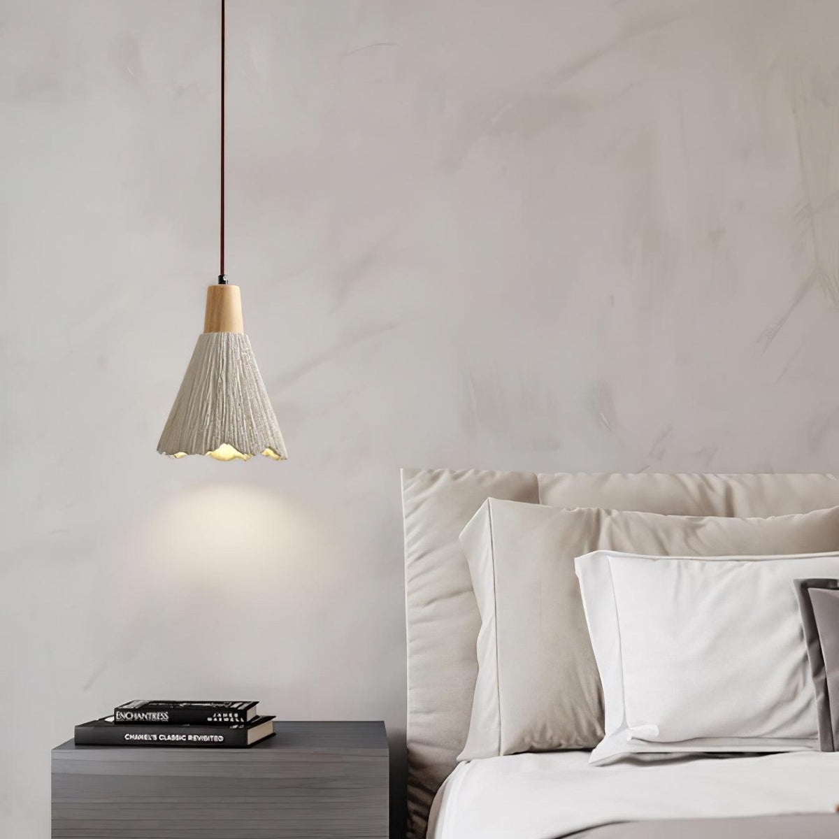 A single bell-shaped Clérachic pendant lights a marbled wall above a dark nightstand and a bed with white pillows.