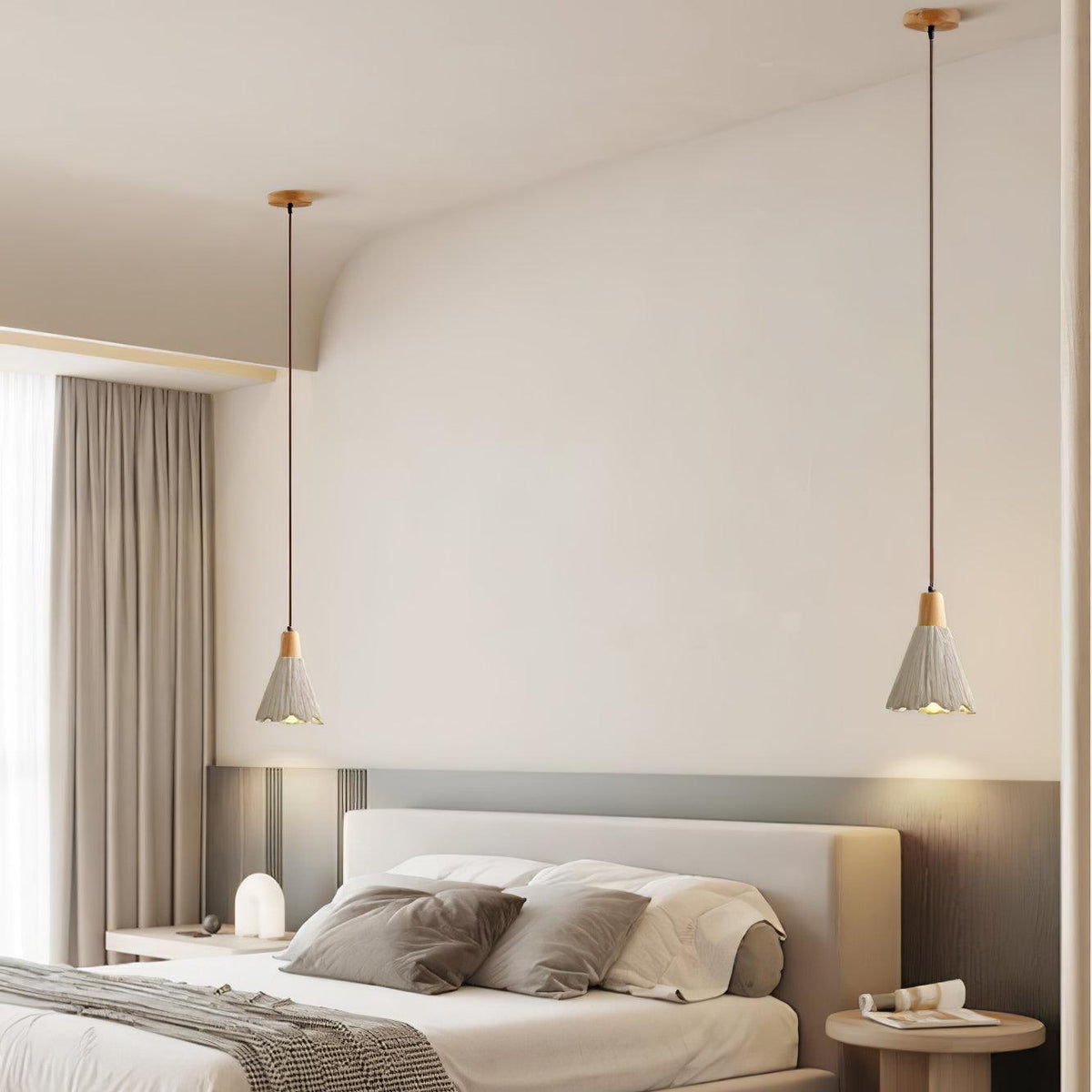 Two bell-shaped Clérachic pendants glow on either side of a bed in a pale bedroom with a lamp on the nightstand.