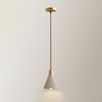 A Clérachic pendant with a bell shade hangs from a round wooden canopy against a plain cream wall, its rim lit warm.