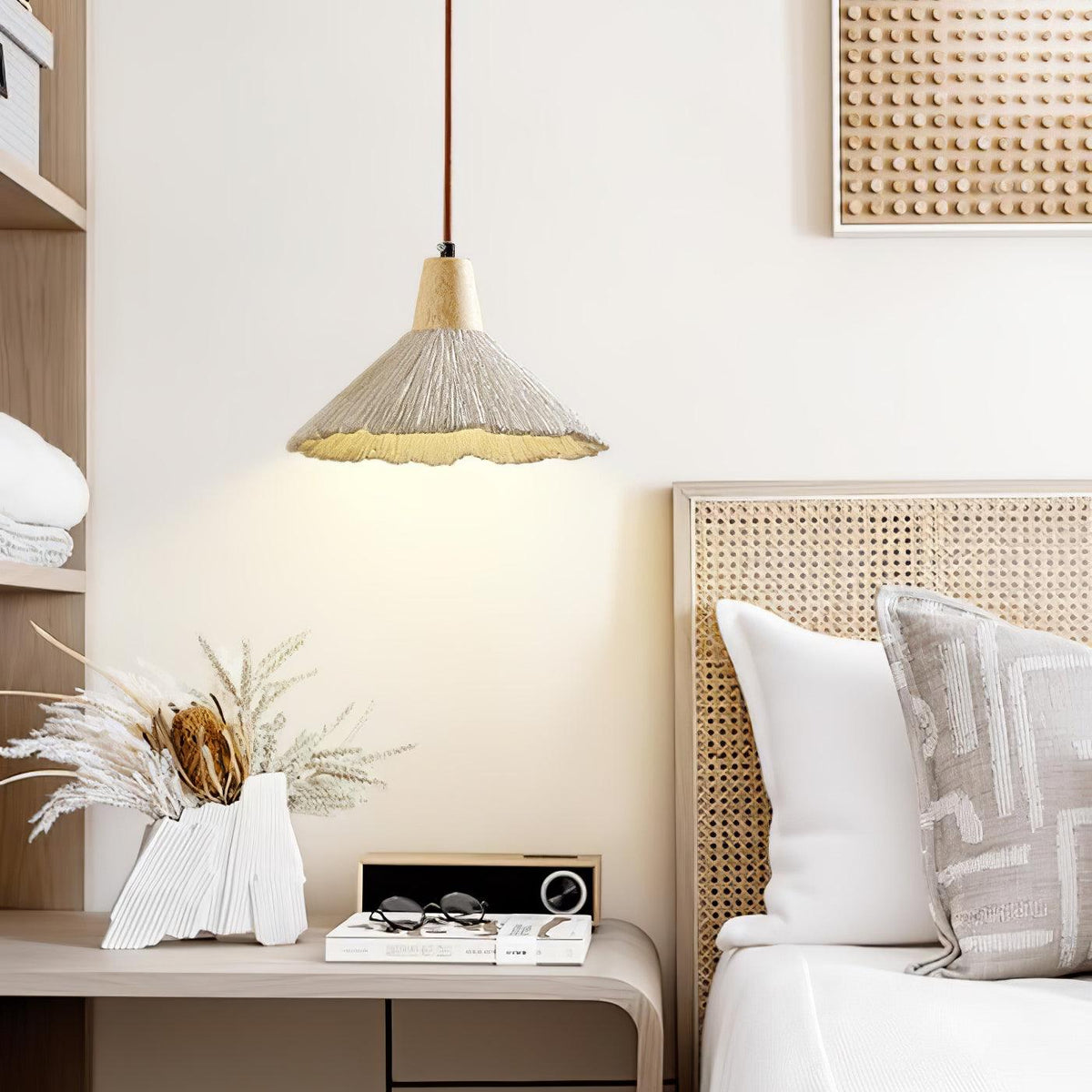 A wide-shade Clérachic pendant hangs by a rattan headboard and a vase of dried grasses on a pale shelf.