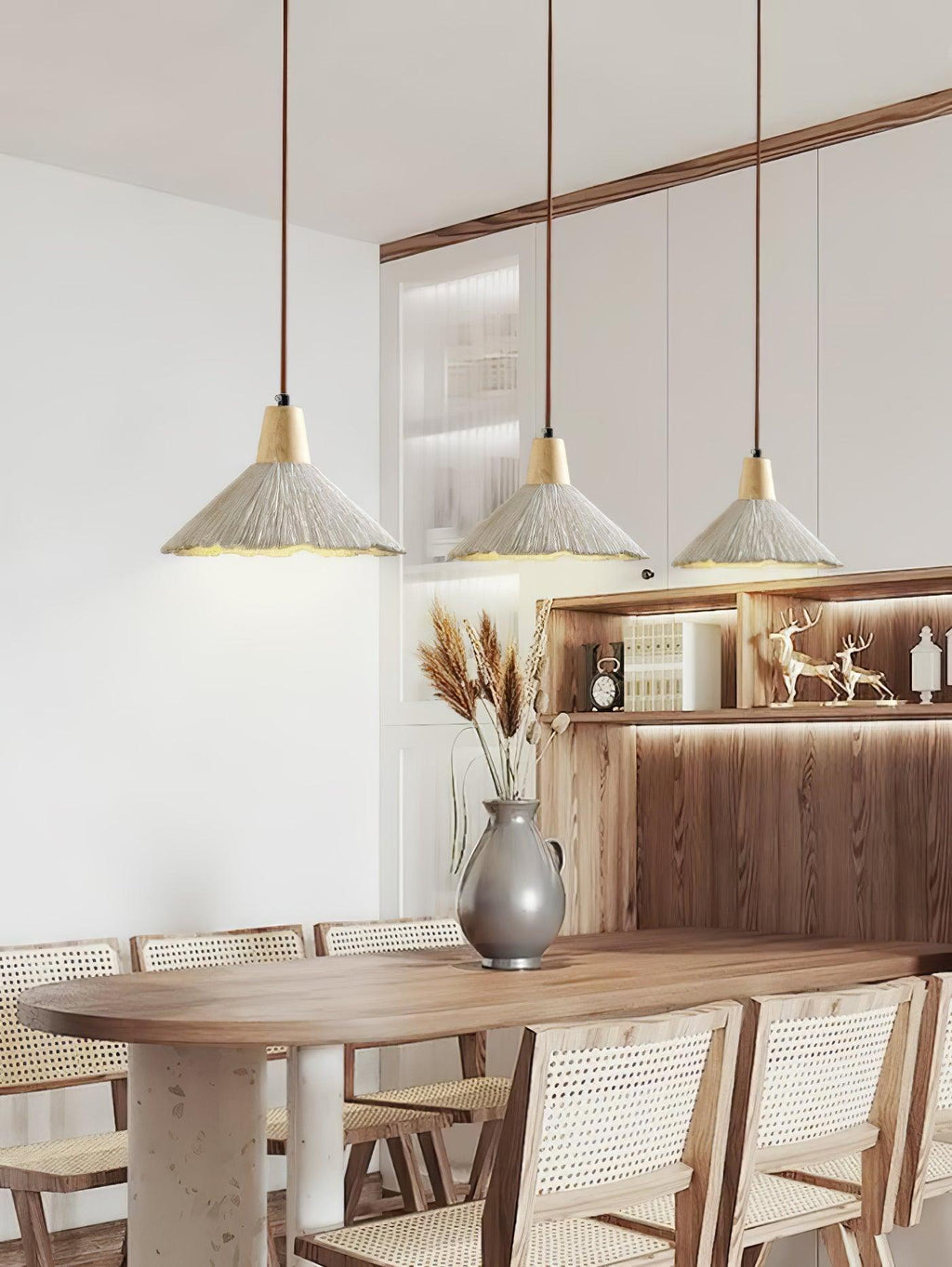 Three wide-shade Clérachic pendants hang in a row over a long dining table with woven chairs and a grey vase.