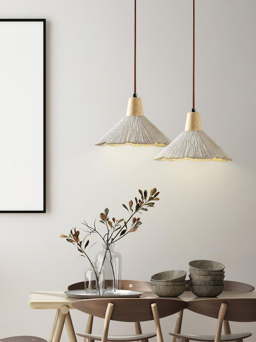 Two wide-shade Clérachic pendants glow above a dining table set with stacked bowls and a vase of branches.