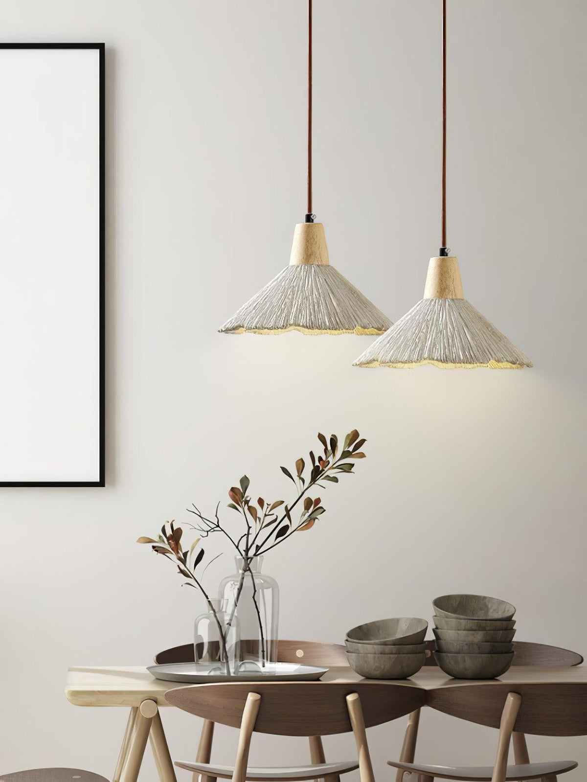 Two wide-shade Clérachic pendants glow above a dining table set with stacked bowls and a vase of branches.